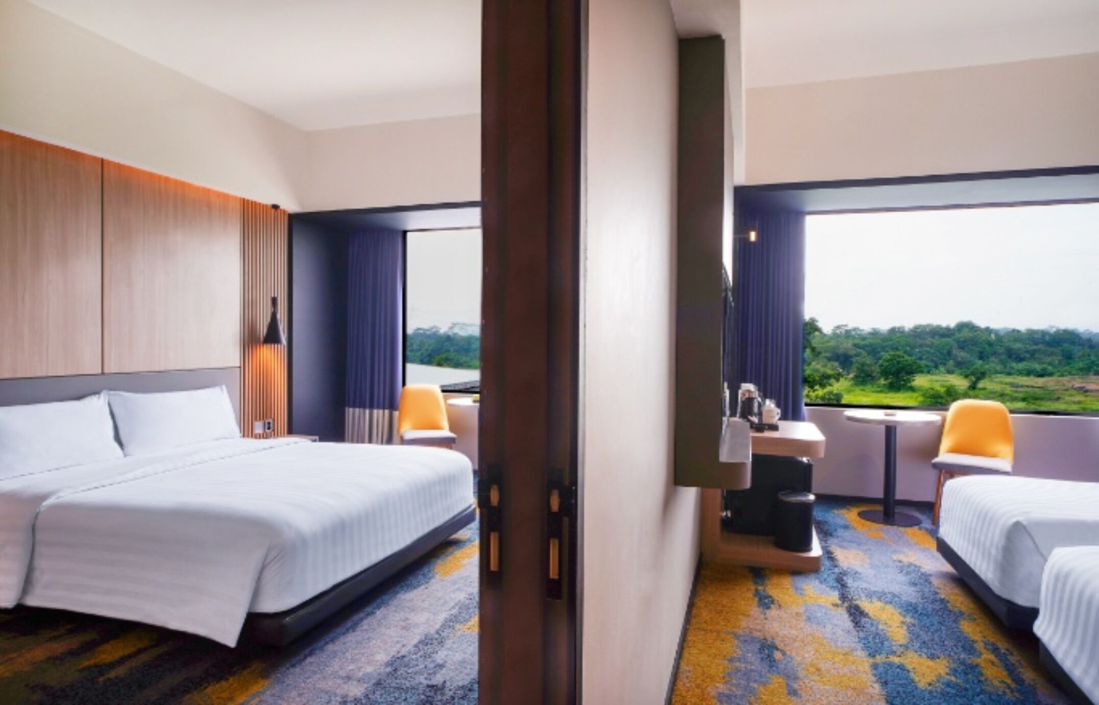 Ein Hotelzimmer mit einem großen Bett, einem Schreibtisch, einem Stuhl und Blick auf eine grüne Landschaft.