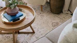 Ein gemütliches Wohnzimmer mit einem runden Holztisch, einem bequemen Sessel und einem kleinen Beistelltisch mit Kerze.
