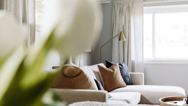 Ein modernes Wohnzimmer mit einer Couch, Kissen, einer Stehlampe und einem Fenster mit Vorhängen.