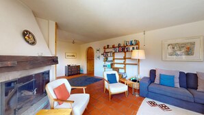 Ein Wohnzimmer mit Kamin, einer Couch, Sesseln, einem Bücherregal und einem Gemälde an der Wand.