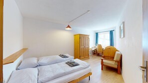 A bedroom with a bed, a wooden wardrobe, a desk with a chair, and a hanging light fixture.
