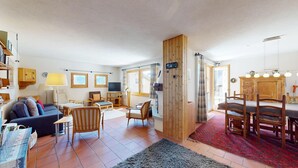 Ein Wohnzimmer mit einer Couch, Sesseln, einem Fernseher, einem Kamin und einem Essbereich mit Tisch und Stühlen.