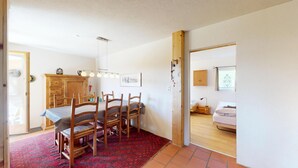 Ein Essbereich mit Holztisch und -stühlen, einem roten Teppich mit Muster, einem Holzkabinett und einer Deckenleuchte.