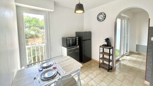 A compact kitchen with a dining area, a microwave, a refrigerator, and a clock on the wall. - Charming Studio for 2 in Ajaccio, Close to Airport and Amenities (Ajaccio)