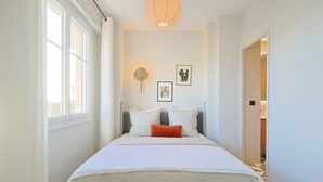 Un dormitorio con una cama grande, una mesita de noche, un ventilador de pared y un cuadro enmarcado.