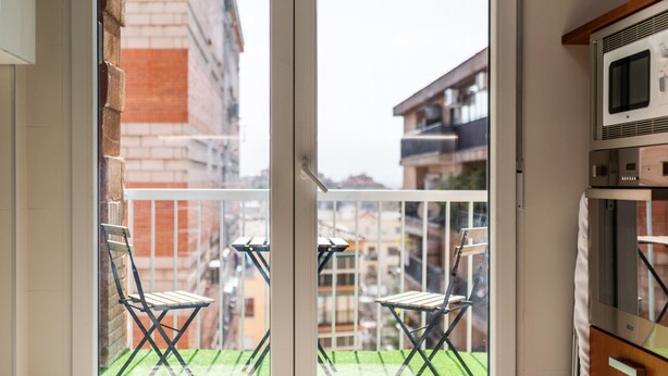 Un balcon avec deux chaises pliantes, une petite table et une vue sur les immeubles voisins.