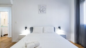 Une chambre d’hôtel avec un grand lit, deux tables de chevet, une œuvre d’art accrochée au mur et une vue sur la salle de bain.