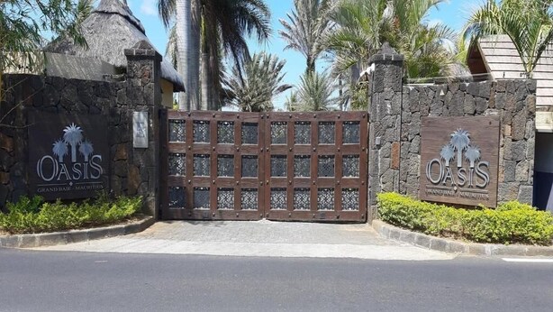 A gated entrance to Oasis Grand Baie, Mauritius, with stone walls and palm trees. - Oasis 1 Villa with 3 Bedrooms  (Grand-Baie)