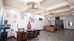 A modern office with a desk, chairs, and a sofa. There is a ceiling fan, a clock, and a television on the wall.