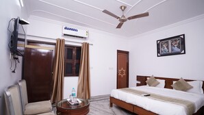 A hotel room with a bed, a chair, a small table, an air conditioner, a ceiling fan, and a window with curtains.
