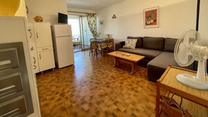 A compact living space with a kitchenette, a dining area, a sofa, and a fan.