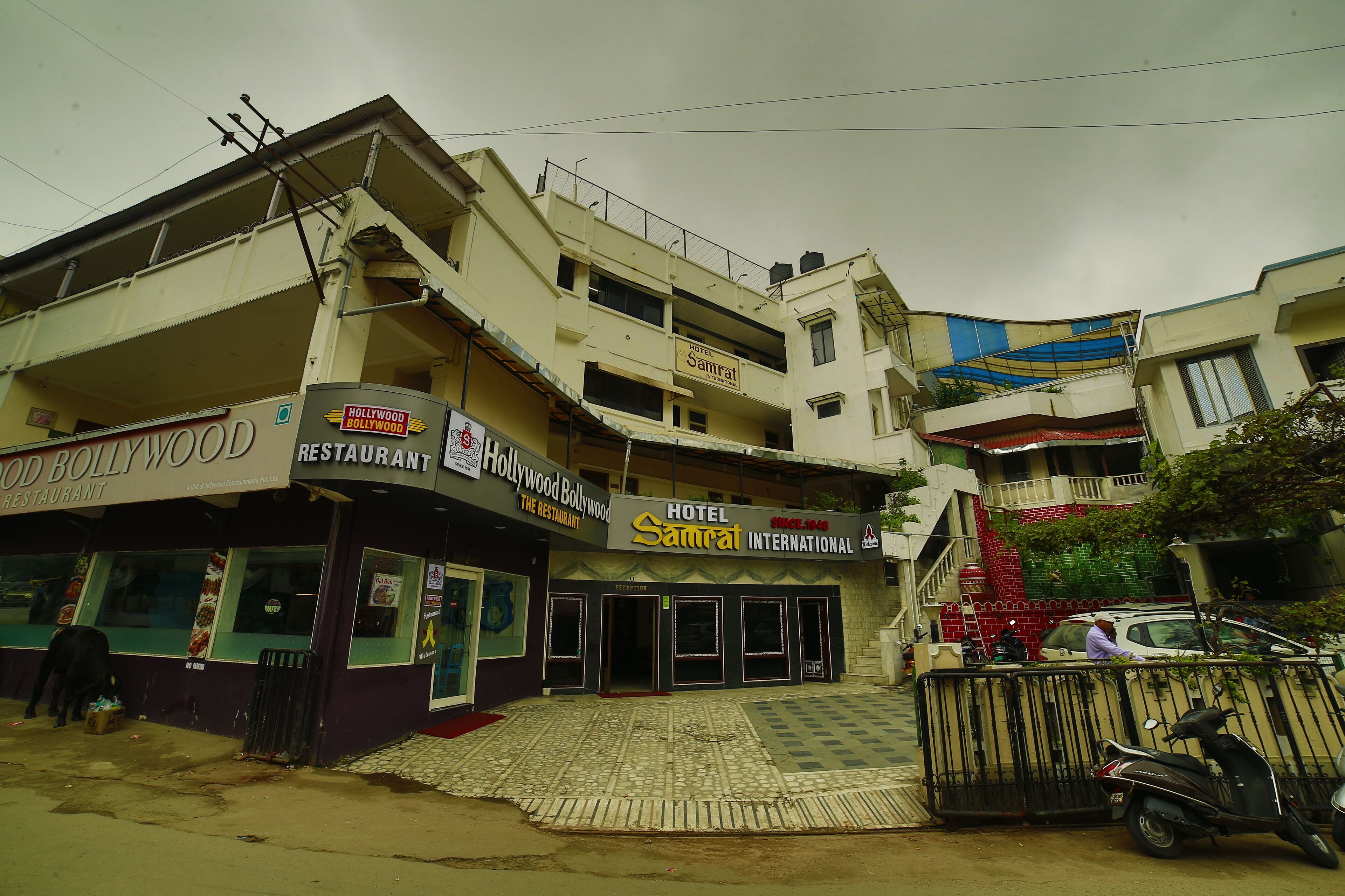 Un edificio de varios pisos con un cartel que dice 'Hotel Samrat International' y 'Hollywood Bollywood Restaurant'.