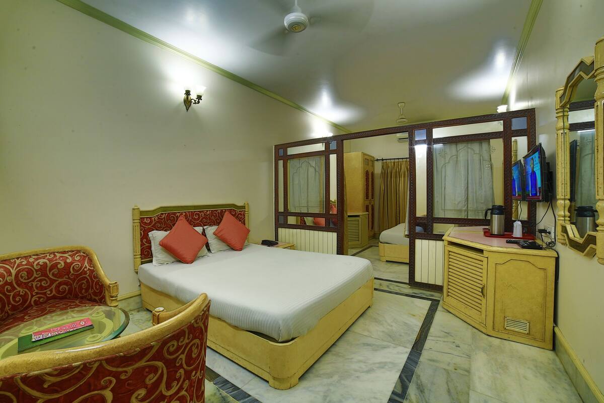 A hotel room with a bed, a sofa, a small table, a mirror, and a television.