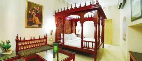 Una habitación tradicional con una cama con dosel, un sofá y una mesa de centro de cristal.
