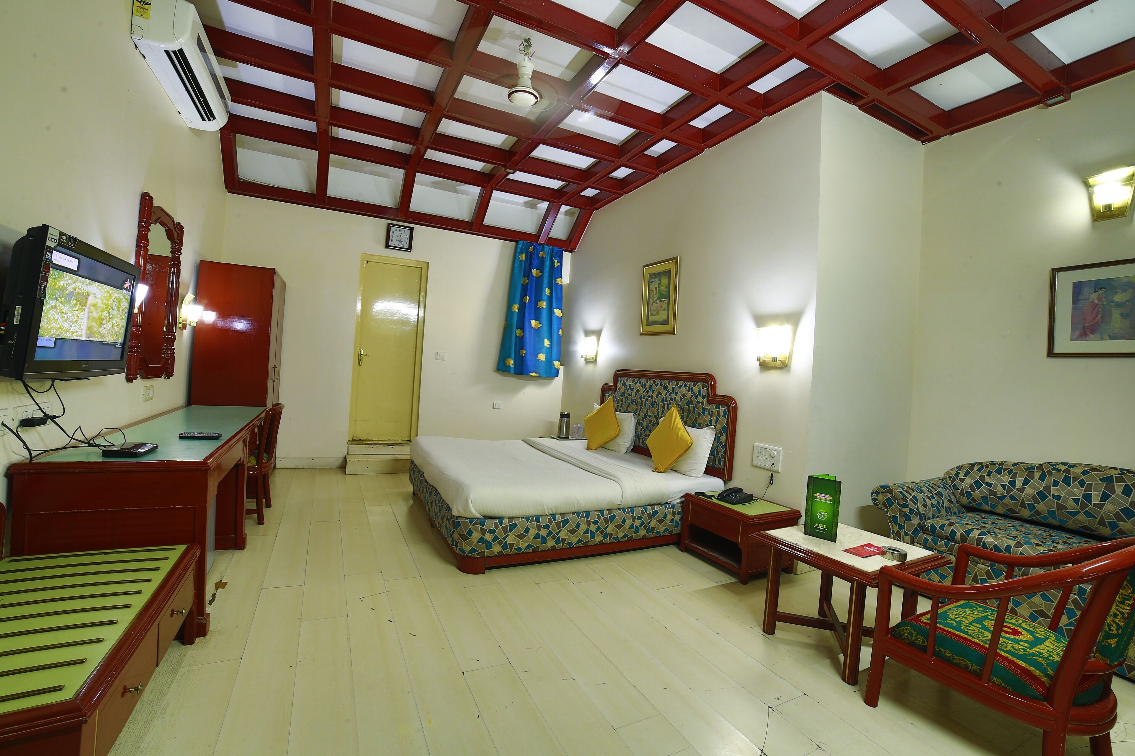 A hotel room with a bed, a desk, a chair, a sofa, a television, and a ceiling fan.