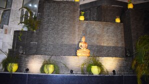 A stone wall with a Buddha statue, potted plants, and a water feature.