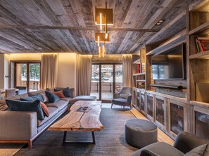 Una sala de estar moderna con techo de madera, un sofá grande, una mesa de centro y una televisión.