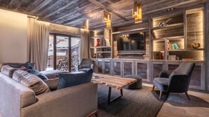 A modern living room with a wooden ceiling, a large TV, and built-in shelves with books and decorative items. - Luxurious 7-room apartment for 14 pers. in Avoriaz with wellness access (Avoriaz)