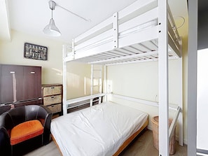 Une chambre avec un lit superposé, un bureau, une chaise et une étag ère fixée au mur.