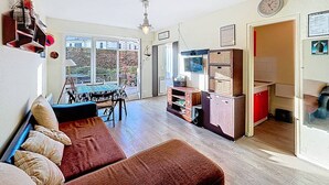 A living room with a sofa, a dining table, and a kitchen area with cabinets and a refrigerator. - Ground Floor Apartment with Terrace, Near Shops, Sleeps 4 (Merville-Franceville-Plage)