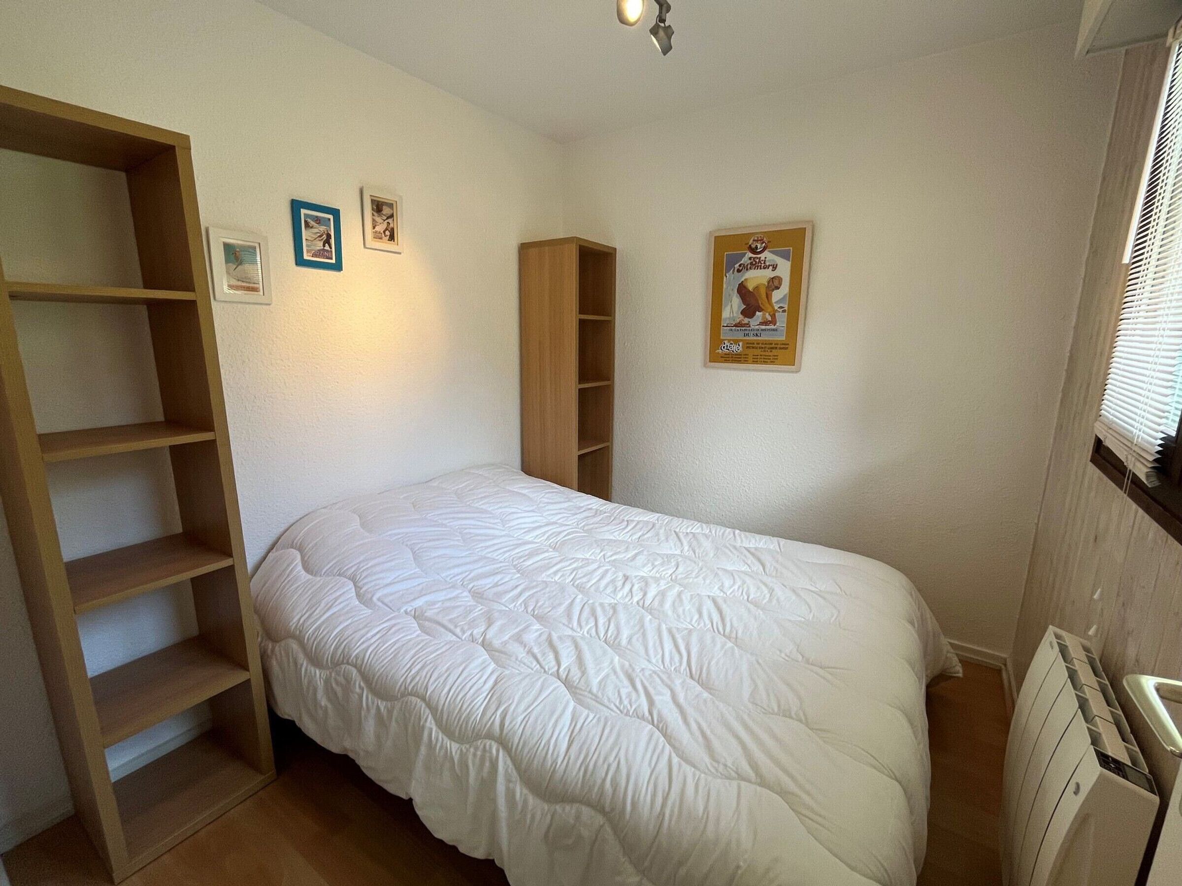 Un dormitorio con una cama, una estantería de madera, un radiador y un cartel en la pared.