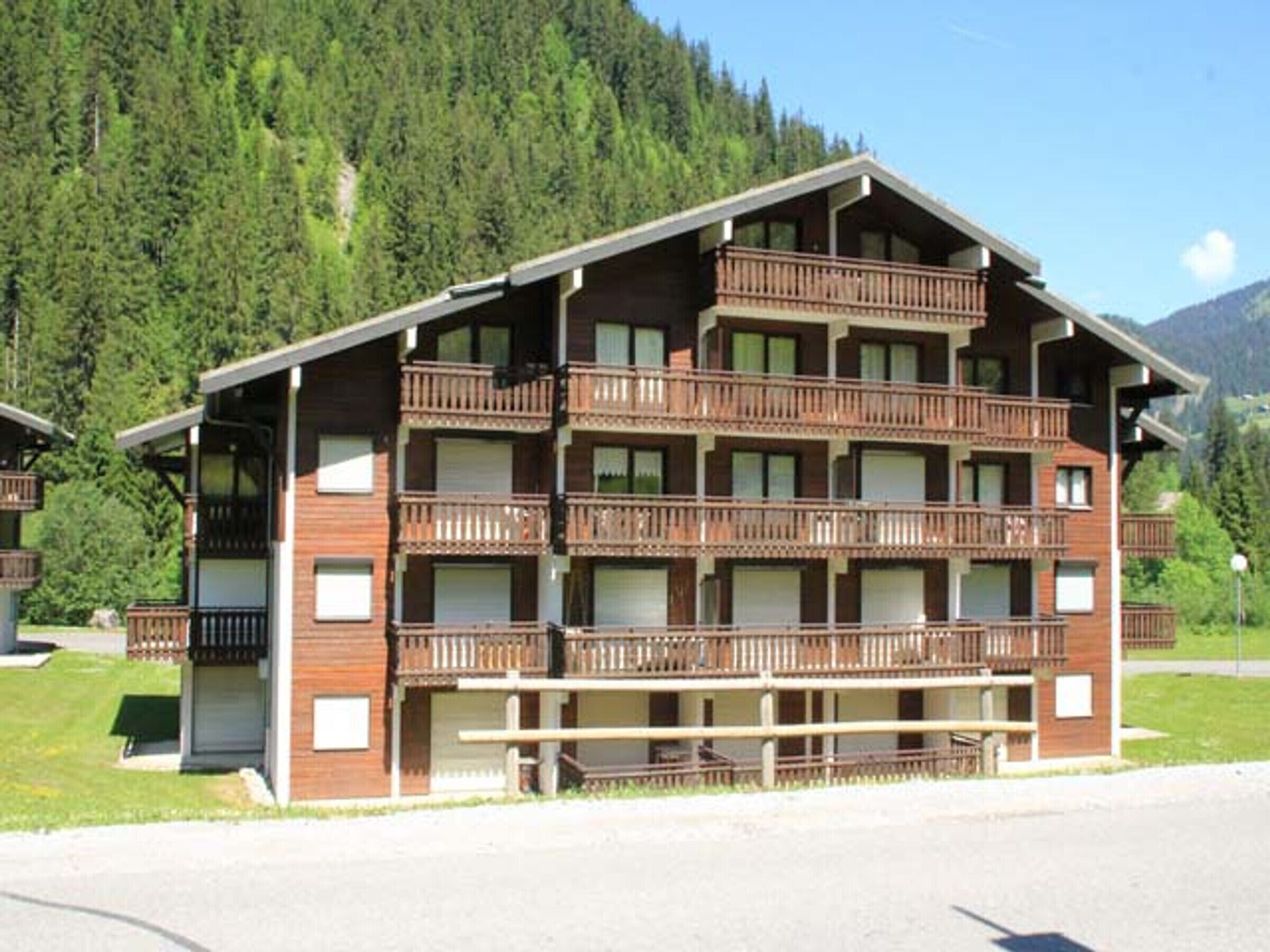 A multi-story building with balconies, set against a mountainous backdrop.