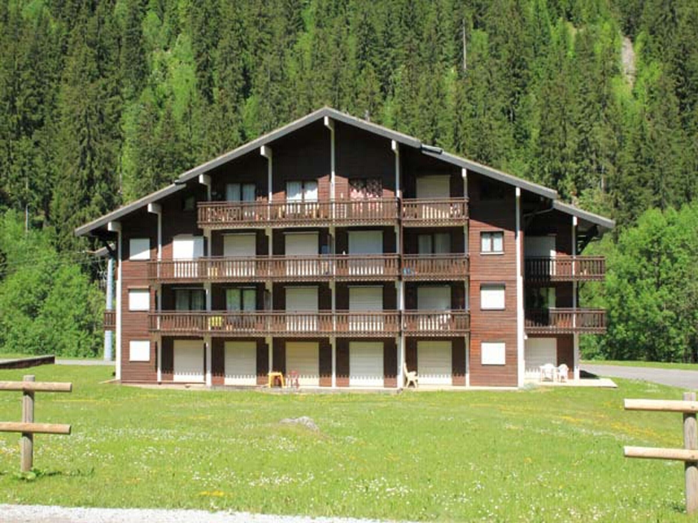 A multi-story building with balconies, set against a forest backdrop.
