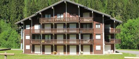 A multi-story building with balconies, set against a forest backdrop.