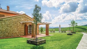 A stone building with a red-tiled roof, a pergola, and a grassy lawn with outdoor seating.