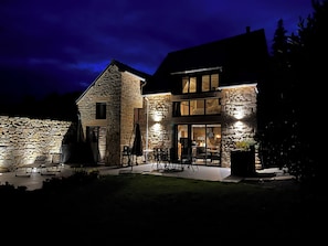A stone house with a patio area, outdoor seating, and a visible interior with a dining area.