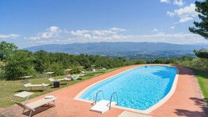 Une piscine rectangulaire à l’eau d’un bleu limpide, entourée d’une terrasse carrelée de couleur rouge. On y trouve des chaises longues et des parasols.