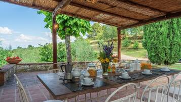 Ein Essbereich im Freien mit einer Holz-Pergola, einem Tisch, der mit weißem Geschirr gedeckt ist, und Blick auf einen üppigen Garten.