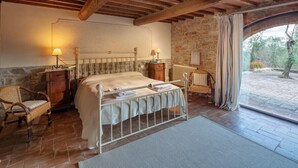 Une chambre à coucher comprenant un lit, deux tables de chevet, une chaise, un radiateur et une vue sur l’extérieur.
