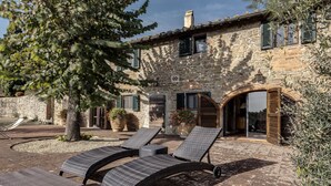 Un bâtiment en pierre doté d’une cour, d’un espace extérieur aménagé pour s’asseoir et d’un grand arbre.