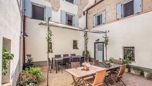 A courtyard with a wooden table and chairs, surrounded by potted plants and a brick floor. - Villa Benedetta - Homelike Villas (Osimo)