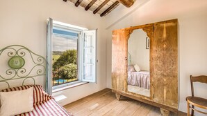 A bedroom with a large window, a bed with striped bedding, a wooden wardrobe, and a mirror reflecting the bed. - Villa Benedetta - Homelike Villas (Osimo)