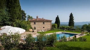 Una casa de piedra con piscina, rodeada de vegetación y montañas al fondo.