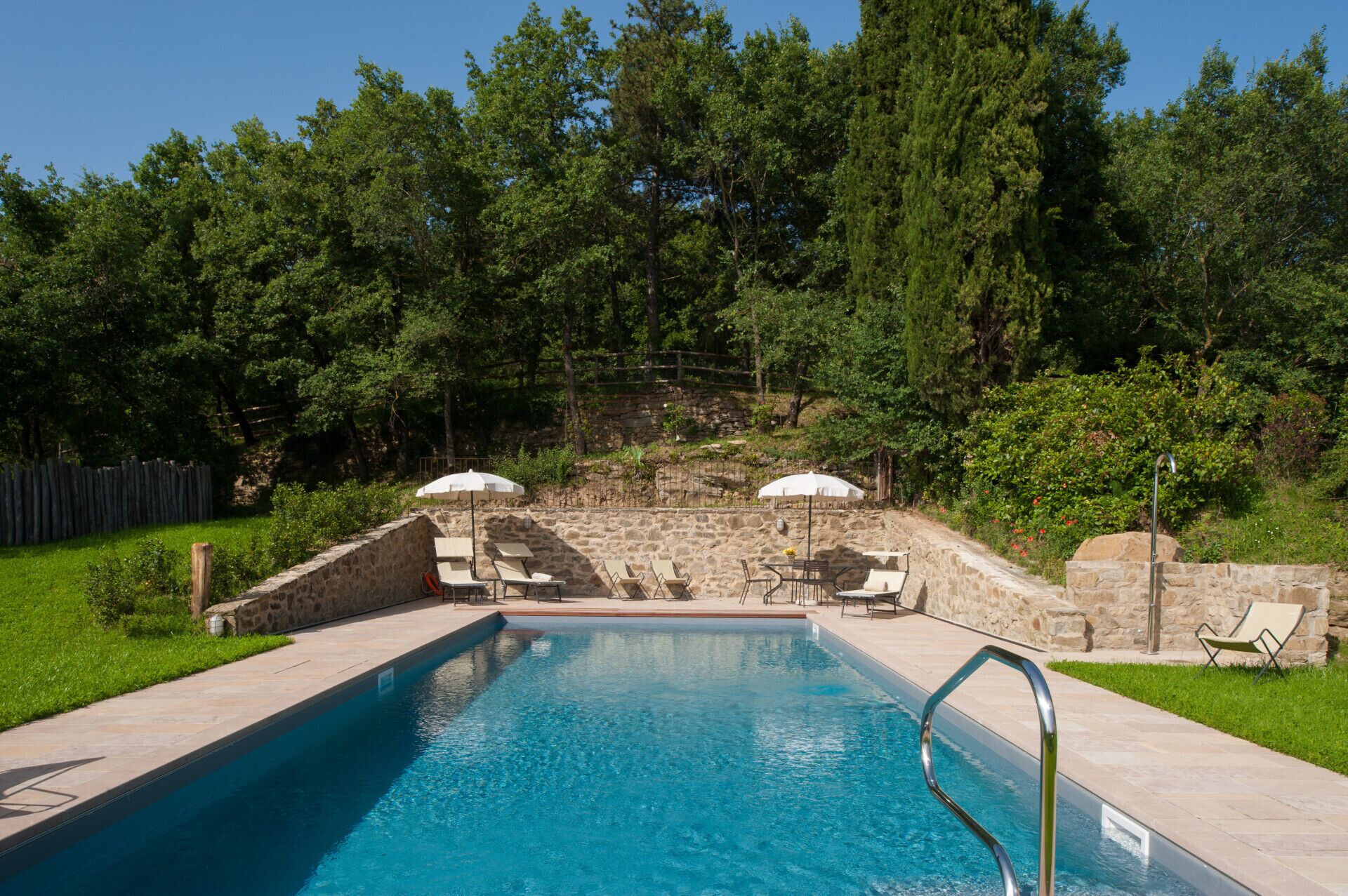 Une piscine avec un mur en pierre et des chaises longues.
