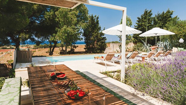 A poolside area with lounge chairs, a table with a bowl of fruit, and a view of the sea. - Villa Calipso - Homelike Villas (Nardò)