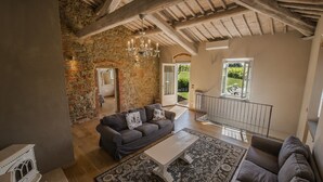 A spacious living room with a stone wall, a grey sofa, a white coffee table, and a patterned rug. - Villa Chianti - Homelike Villas (Terranuova Bracciolini)