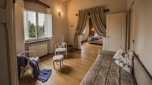 A cozy room with a wooden floor, a bed with curtains, a chair, a sofa, and a window with a view of trees. - Villa Chianti - Homelike Villas (Terranuova Bracciolini)