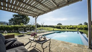 A pool area with a pergola, lounge chairs, and a table with drinks and flowers. - Villa Chianti - Homelike Villas (Terranuova Bracciolini)