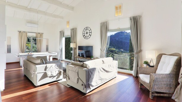Een ruime woonkamer met een groot raam met uitzicht op de bergen, een flatscreen televisie en een eethoek met een tafel en stoelen.