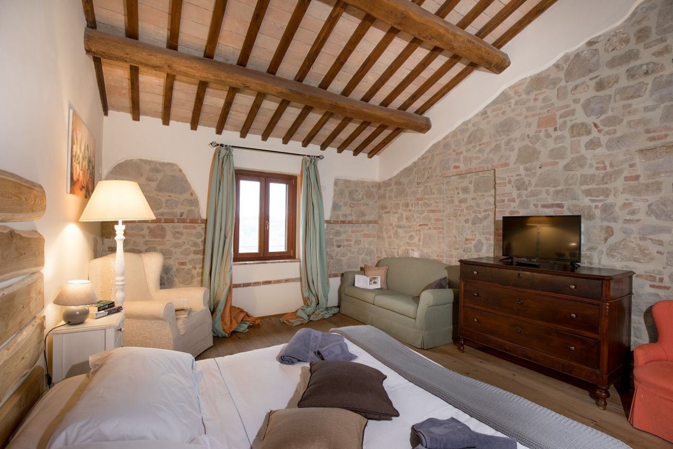 A cozy room with a bed, a wooden dresser, a television, and a stone wall.
