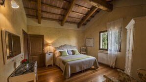 Un dormitorio con techo de madera, una cama con cabecera floral, una mesita de noche, una silla y una ventana con cortinas.