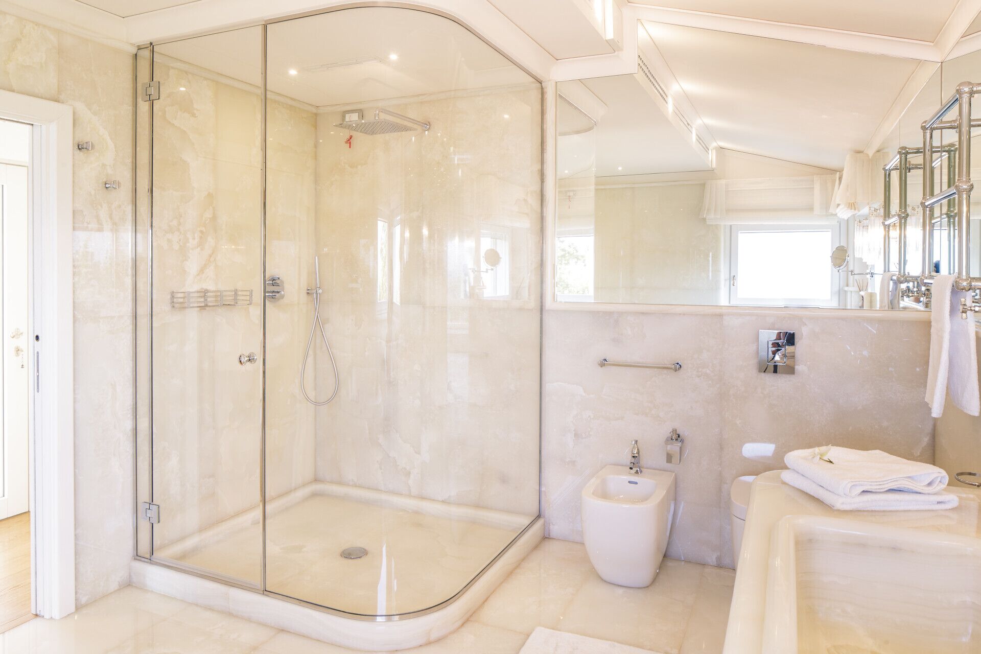 Ein modernes Badezimmer mit einer gläsernen Duschkabine, einem Bidet und einem Waschtisch mit Spiegel.
