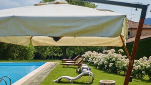 Un espace aménagé au bord de la piscine, avec une table dressée pour le thé, des chaises longues et un jardin fleuri.