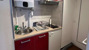A compact kitchen with a sink, a dish rack, and a red cabinet. - Cozy Studio for 2 Near Beach with Private Parking (Cap d'Agde)
