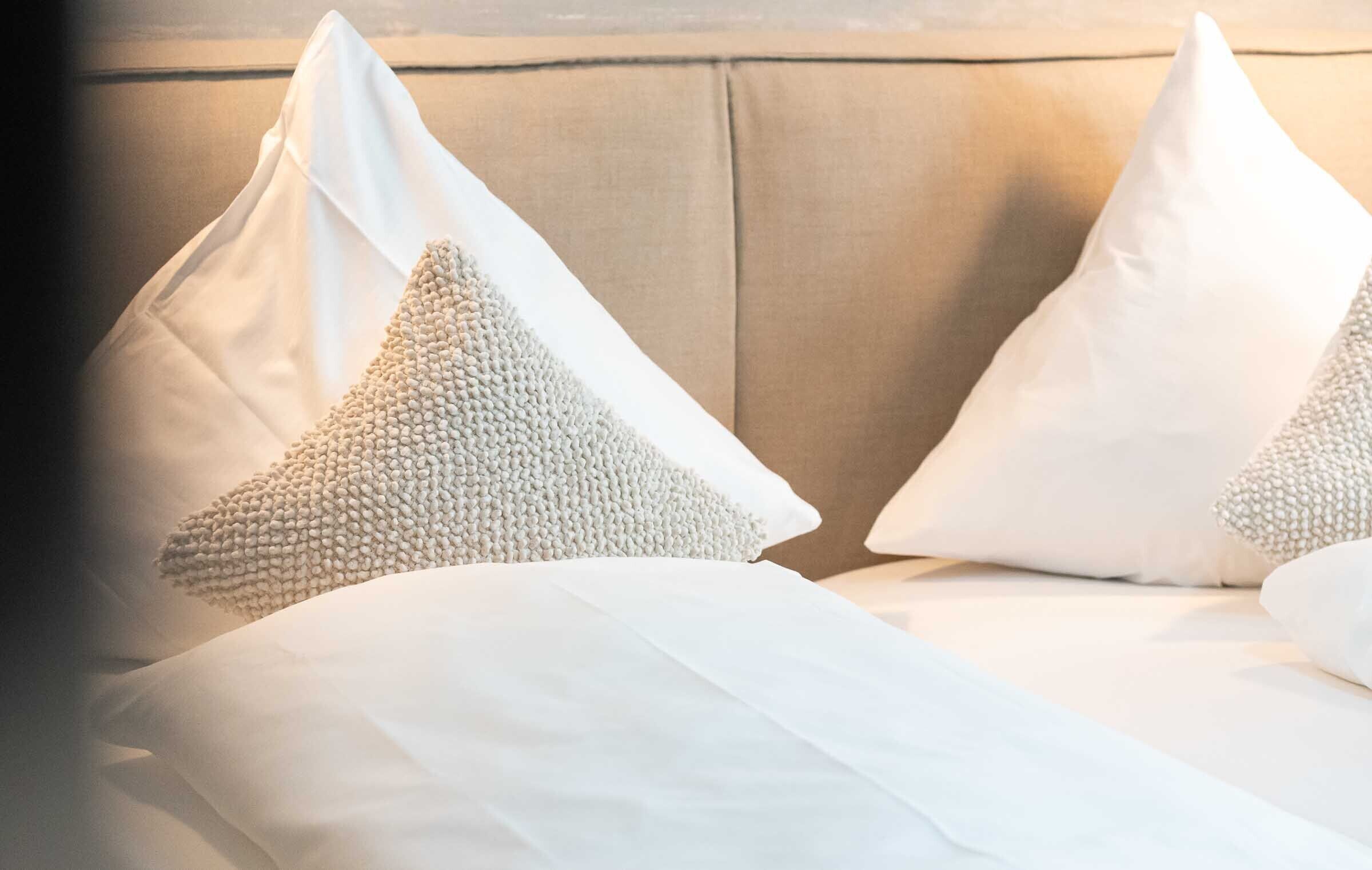 A bed with white linens and two decorative pillows.