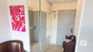 A hallway with a brown leather chair, a red abstract painting, and a door with a mirror. - Cozy Studio for 2 with A/C, Pool Access, & Parking in Agde (Cap d'Agde naturisme)